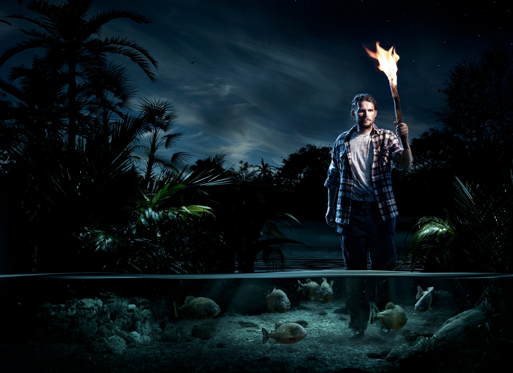 A nighttime scene where a person is standing in front of a body of water, holding a burning torch high. The sky is dark with stars and clouds, and there are palm trees in the background. Under the water surface, you can see piranhas and aquatic plants. The photo is interesting because it shows a contrast between the fiery torch above the water and the calm underwater environment.